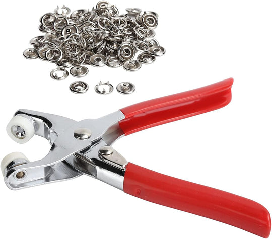 Red-handled snap fastener pliers beside a pile of silver press-stud buttons