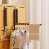 Over-door rack holding hangers of clothes and a towel on a wooden door